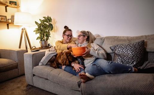 A couple eating popcorn on the couch with their dog